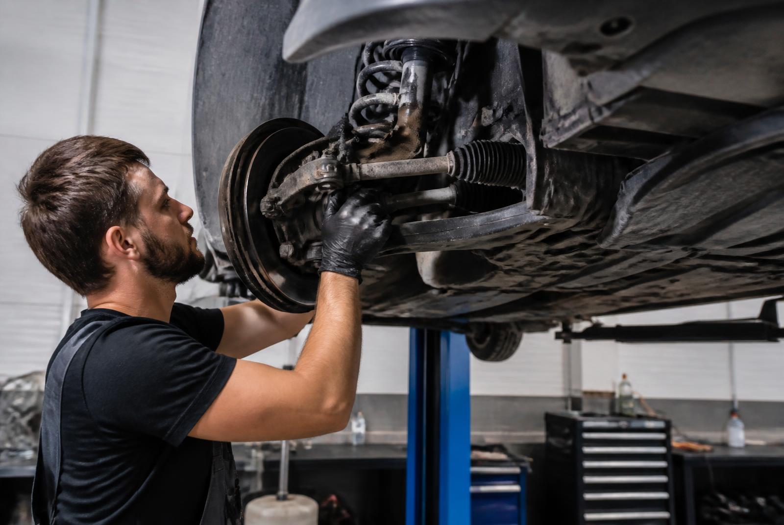Technician servicing front strut, control arm and steering components on a raised vehicle